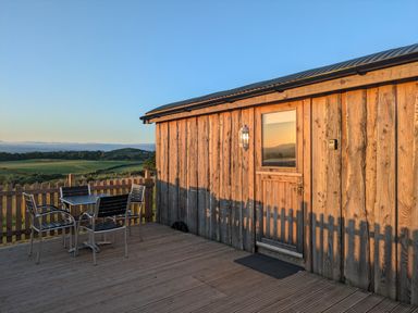 A wooden deck with a table and four chairs outside a wooden building at Hafan Gelli Sheperds Hut - Enlli in Pwllheli