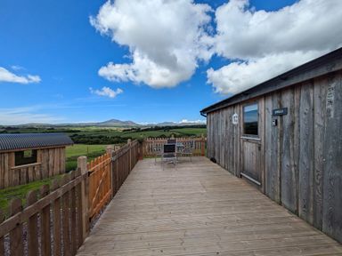 An outdoor wooden deck with table and chairs beside a wooden building at Hafan Gelli Sheperds Hut - Enlli in Pwllheli