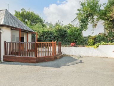 An outdoor area with a small wooden deck and railing next to a white wall with plants and flowers at Little Trevallan in Looe