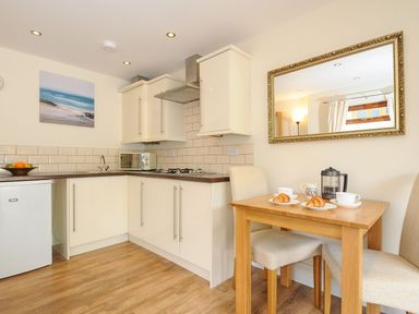 A kitchen with white cabinets a small dining table with two chairs and croissants on plates at Little Trevallan in Looe