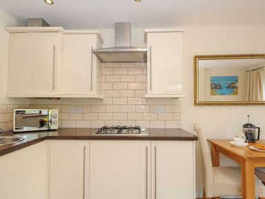 A kitchen with cream cabinets a gas stove a microwave and a wooden table with two chairs at Little Trevallan in Looe