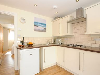 A kitchen with white cabinets a brown countertop a small white fridge a microwave and a bowl of fruit at Little Trevallan in Looe