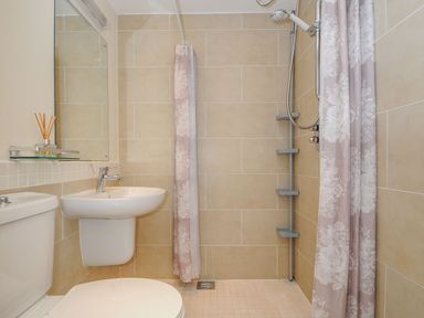 A bathroom with a toilet sink mirror and shower area with floral curtain at Little Trevallan in Looe