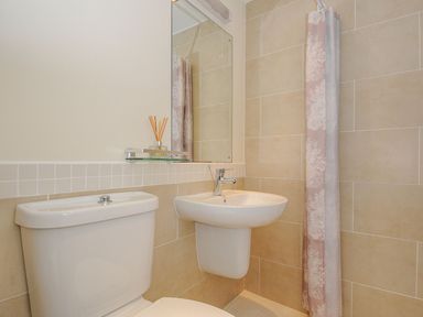 A bathroom with a toilet sink mirror and floral shower curtain at Little Trevallan in Looe