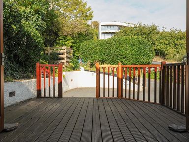 A wooden deck with a gate and surrounding greenery at Little Trevallan in Looe