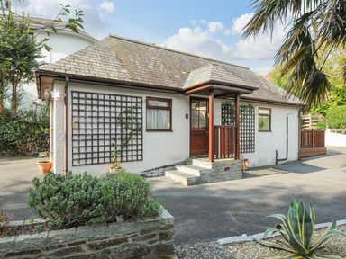 A single-story house with a tiled roof and wooden porch surrounded by plants at Little Trevallan in Looe