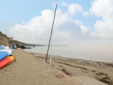 A beach with sand and kayaks near a stone wall and a person walking at Little Trevallan in Looe