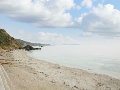 A beach with rocks and cliffs along the shore under a cloudy sky at Little Trevallan in Looe