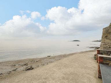 A sandy and rocky shoreline with calm water and an island in the distance at Little Trevallan in Looe