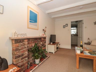 A living room with a brick fireplace plant TV on a stand wooden coffee table and beige sofa at Shell Seeker Cottage in Sewerby