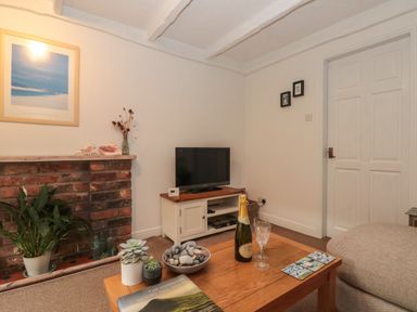 A living room with a wooden coffee table holding plants a bottle of cava and two glasses next to a beige sofa at Shell Seeker Cottage in Sewerby