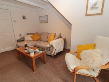 A living room with a sofa, armchair, wooden coffee table, and wall art at Shell Seeker Cottage in Sewerby