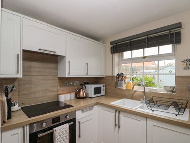 A kitchen with white cabinets a stovetop oven microwave sink and a window at Shell Seeker Cottage in Sewerby