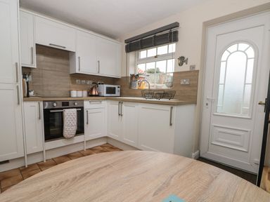 A kitchen with white cabinets a microwave oven kettle and a window next to a white door at Shell Seeker Cottage in Sewerby