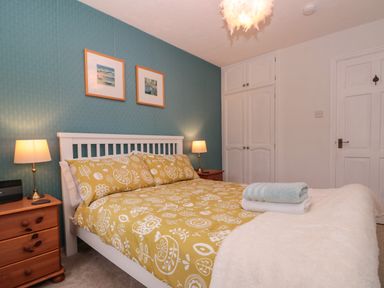A bedroom with a double bed with yellow patterned bedding two bedside tables with lamps and built in white wardrobes at Shell Seeker Cottage in Sewerby