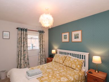 A bedroom with a bed yellow patterned bedding two bedside tables with lamps and a window with curtains at Shell Seeker Cottage in Sewerby