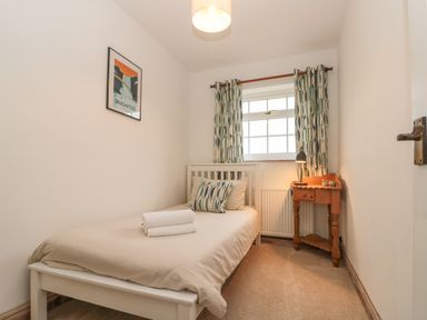 A small bedroom with a single bed a patterned cushion curtains a wooden bedside table with a lamp and a framed picture on the wall at Shell Seeker Cottage in Sewerby
