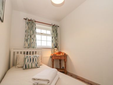 A small bedroom with a single bed, patterned curtains, a wooden side table with a lamp and two small decorative items at Shell Seeker Cottage in Sewerby