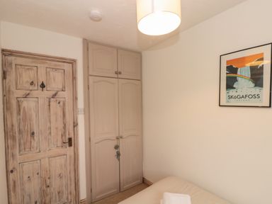 A bedroom corner with a wooden door a built in wardrobe a bed with towels and a framed poster on the wall at Shell Seeker Cottage in Sewerby