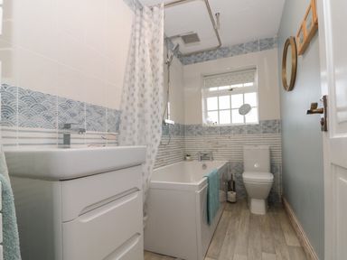 A bathroom with a bathtub shower combination sink toilet window and patterned tiles at Shell Seeker Cottage in Sewerby