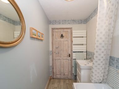 A bathroom with a wooden door a white sink a bathtub with a polka dot shower curtain and a round mirror on the wall at Shell Seeker Cottage in Sewerby