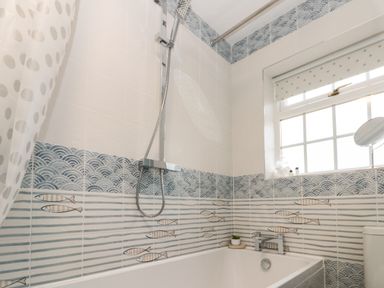 A bathroom with a bathtub shower and window with patterned tiles with fish design at Shell Seeker Cottage in Sewerby