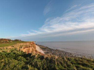 A coastal cliff with grass overlooking a rocky shore and calm sea at Shell Seeker Cottage in Sewerby