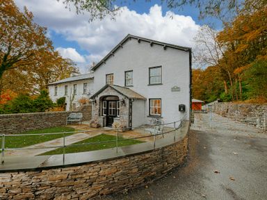 The exterior of a white house with stone walls and a pathway surrounded by trees at Gate House in Coniston