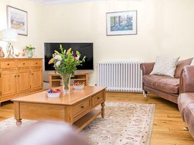 A living room with a wooden coffee table with flowers on it and a television at Gate House in Coniston