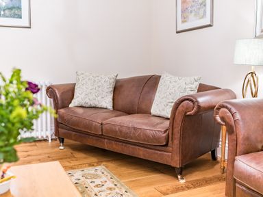 A leather sofa with cushions in a living room with wooden floor and a table with flowers at Gate House in Coniston