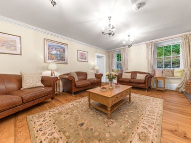 A living room with three brown leather sofas a wooden coffee table a floral rug paintings on the wall and windows with curtains at Gate House in Coniston