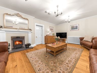 A living room with a fireplace a wooden coffee table a rug leather sofas a television and wooden cabinet at Gate House in Coniston
