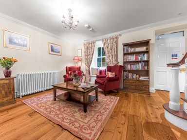 A sitting room with wooden floor red armchairs wooden coffee table with flowers bookshelf and window at Gate House in Coniston