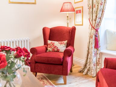 A red armchair with a floral cushion next to a floor lamp and floral curtains at Gate House in Coniston
