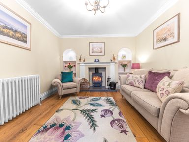 A living room with a sofa and armchair facing a wood burning stove and fireplace at Gate House in Coniston