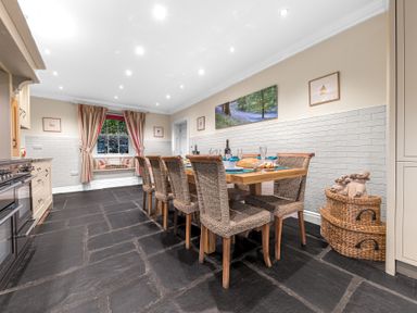A dining area with a wooden table and wicker chairs next to a window with curtains and a built-in bench at Gate House in Coniston