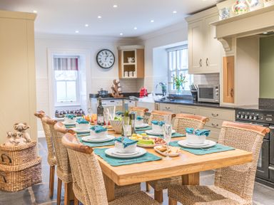 A kitchen with a wooden dining table set with dishes and wicker chairs at Gate House in Coniston