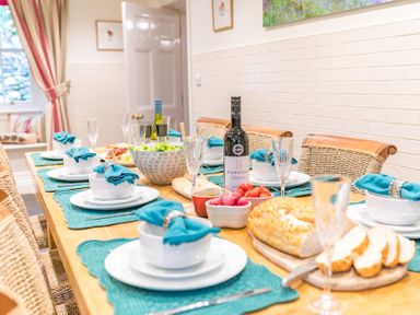 A dining table set with plates bowls teal napkins wine glasses a bottle of wine bread and salad at Gate House in Coniston