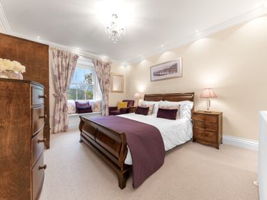 A bedroom with a wooden bed, nightstands, armchair, window with floral curtains and a chest of drawers at Gate House in Coniston