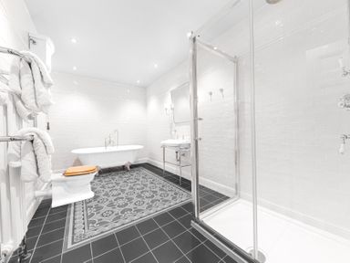 A bathroom with a clawfoot bathtub a toilet with a wooden seat a sink a glass shower enclosure and a black and patterned tile floor at Gate House in Coniston