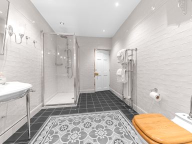 A bathroom with a walk-in shower sink toilet with wooden seat and towel rack at Gate House in Coniston