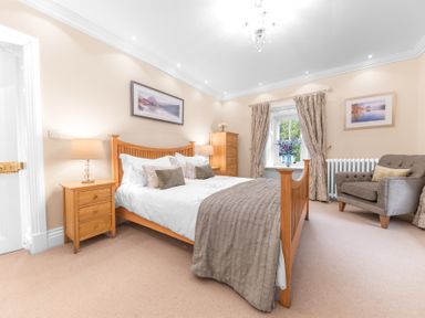 A bedroom with a wooden double bed bedside tables a chest of drawers an armchair and a window at Gate House in Coniston