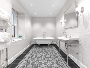 A bathroom with a freestanding bathtub a patterned tile floor a sink with a mirror and wall lights at Gate House in Coniston