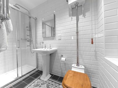 A bathroom with a shower enclosure a pedestal sink a toilet with a wooden seat and white tiled walls at Gate House in Coniston