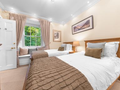 A bedroom with two single beds a window seat with cushions and a lamp at Gate House in Coniston