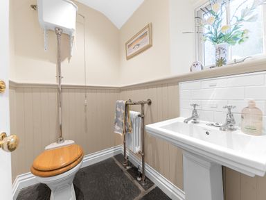 A bathroom with a toilet with a wooden seat a sink with taps a towel hanging on a rail and a window with flowers on the sill at Gate House in Coniston