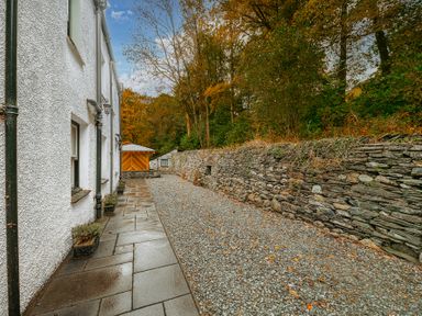A stone pathway next to a white building and a stone wall with trees in the background at Gate House in Coniston