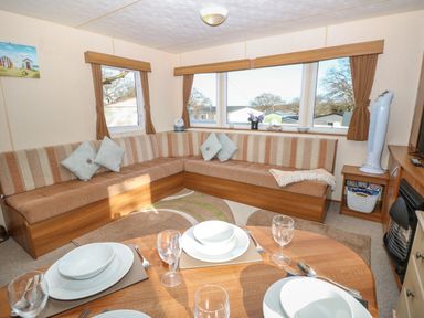 A seating area with striped cushions and pillows around windows with curtains next to a dining table set with plates and glasses at 15 Rosewood Great Thorness near Northwood Isle Of Wight