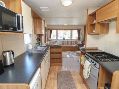 A kitchen area with appliances and a sink leading to a dining space with a sofa and windows at 15 Rosewood Great Thorness near Northwood Isle Of Wight