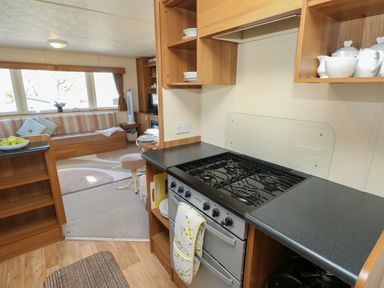 A kitchen area with a stove and countertop leading to a living room with a sofa and windows at 15 Rosewood Great Thorness near Northwood Isle Of Wight